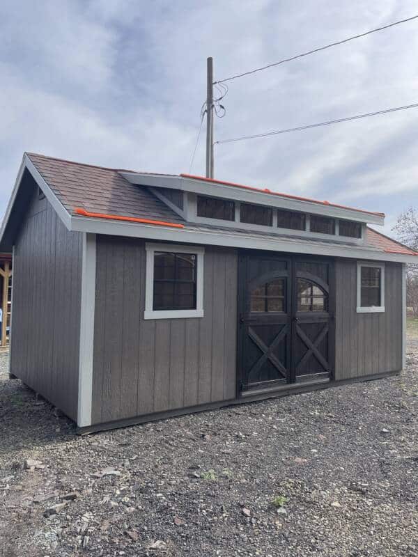 Front view of a 12x20 Smartside Classic A-Frame shed in Barnwood Gray and Gap Gray with Harvard Slate roof, black double round top doors, two black-trimmed windows, and a five-window black dormer.